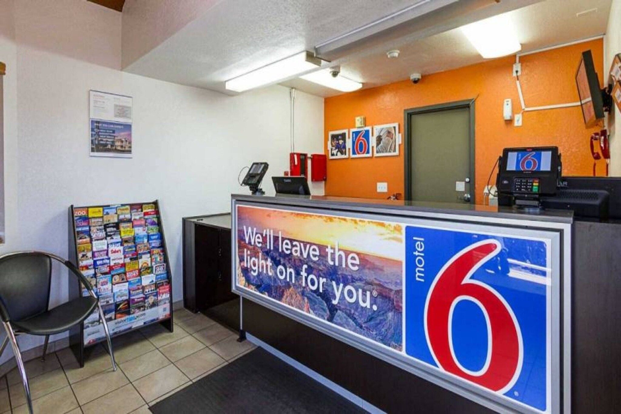A reception desk with a sign advertising a motel, a telephone, a magazine rack, and a chair.