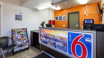 A reception desk with a sign advertising a motel, a telephone, a magazine rack, and a chair.
