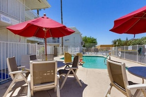 Un espace aménagé au bord de la piscine, avec des chaises longues et des parasols, une piscine et une zone délimitée par une clôture.