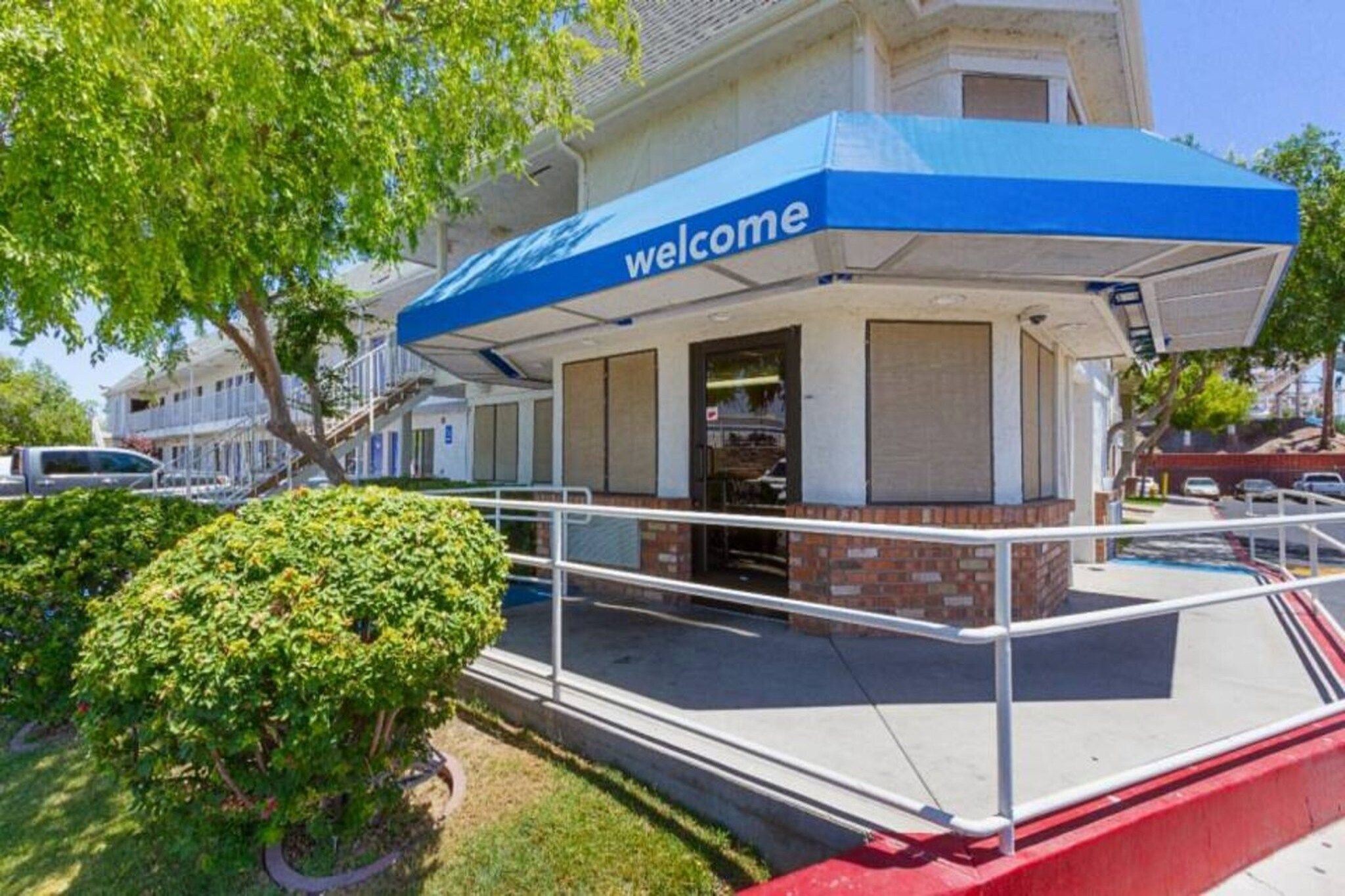 A building with a blue awning and a 'welcome' sign, a gated entrance, and a small garden area.