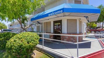 A building with a blue awning and a 'welcome' sign, a gated entrance, and a small garden area.