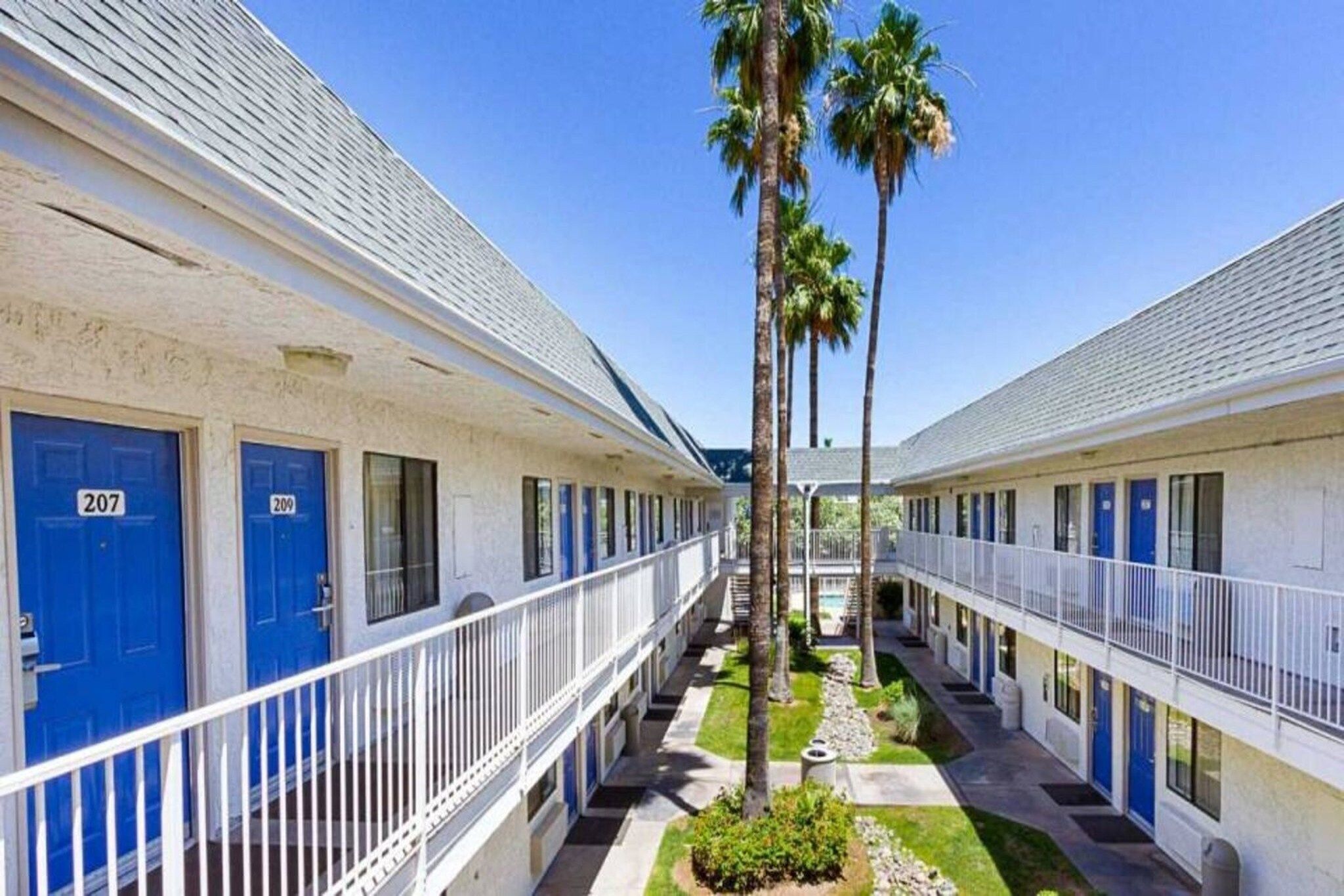 A row of motel rooms with blue doors, numbered 207 and 209, and a central walkway with palm trees.