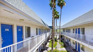 A row of motel rooms with blue doors, numbered 207 and 209, and a central walkway with palm trees.