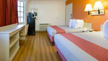 A hotel room with two beds, a desk, a chair, a heater, and a window with curtains.