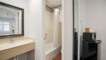 Un baño con lavamanos, espejo, ducha y microondas.