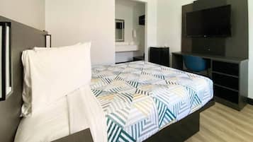 A hotel room with a bed, a desk, a chair, a television, and a mirror.