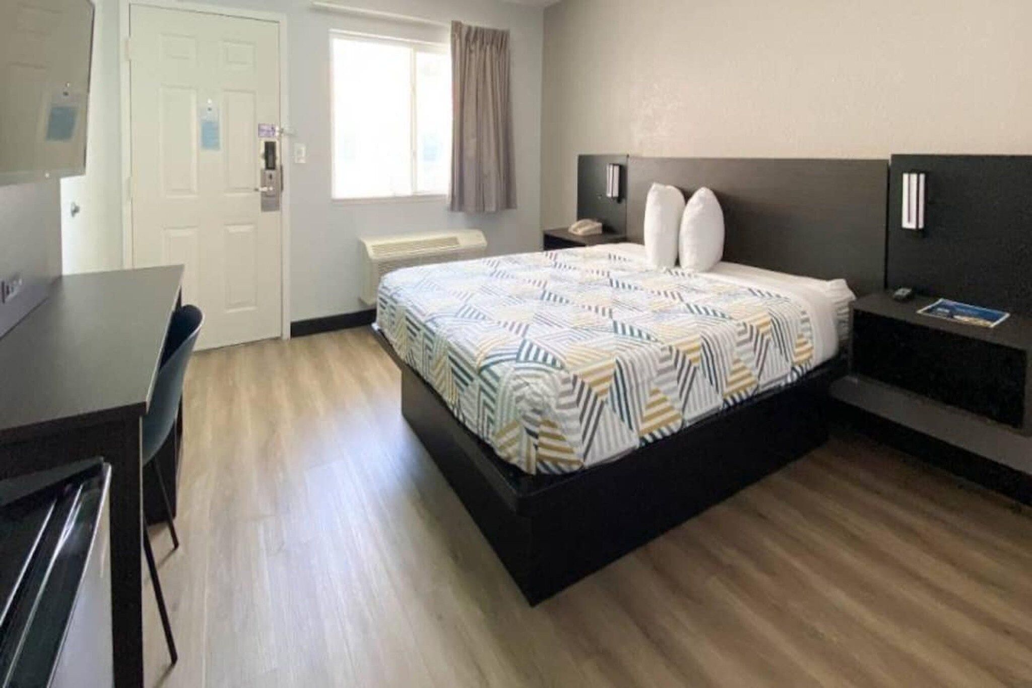 Habitación de hotel con cama, mesita de noche, lámpara y escritorio con sillas.