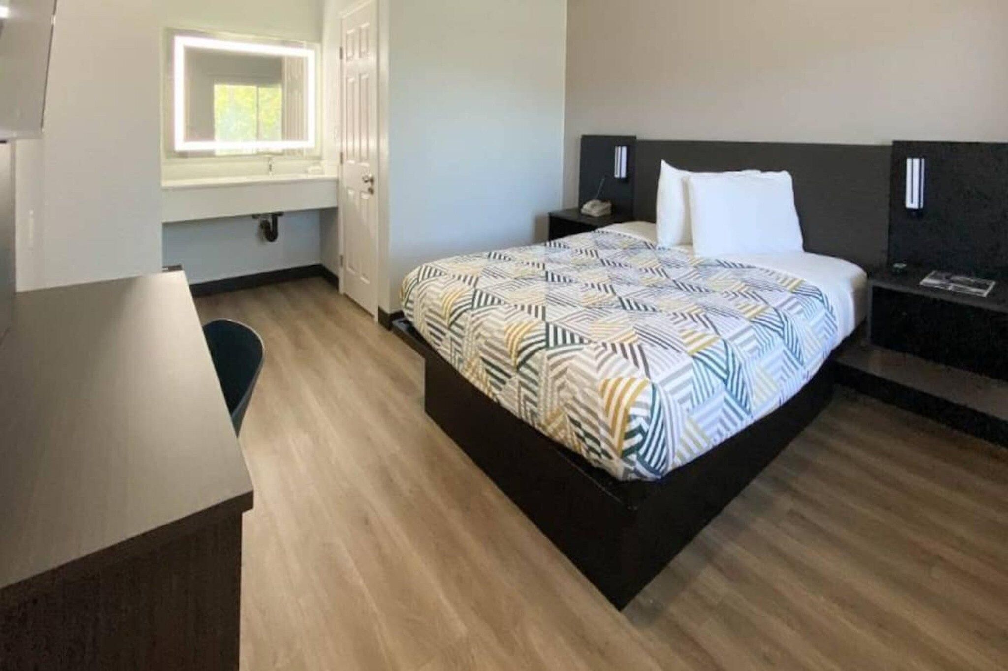 A hotel room with a bed, bedside tables, a desk, and a window.