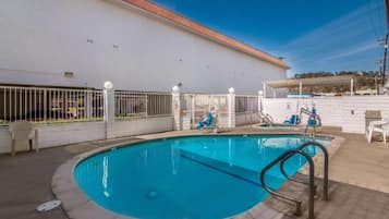 Una piscina con un muro bianco e un tetto piastrellato sullo sfondo.