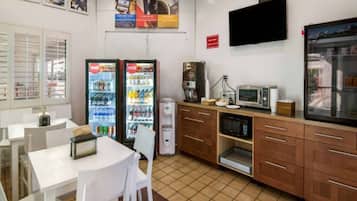 A small kitchenette with a refrigerator, microwave, coffee maker, and a single table with chairs.