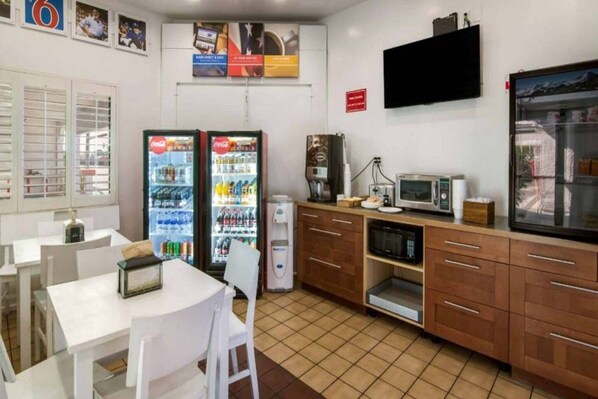A small kitchenette with a refrigerator, microwave, coffee maker, and a single table with chairs.
