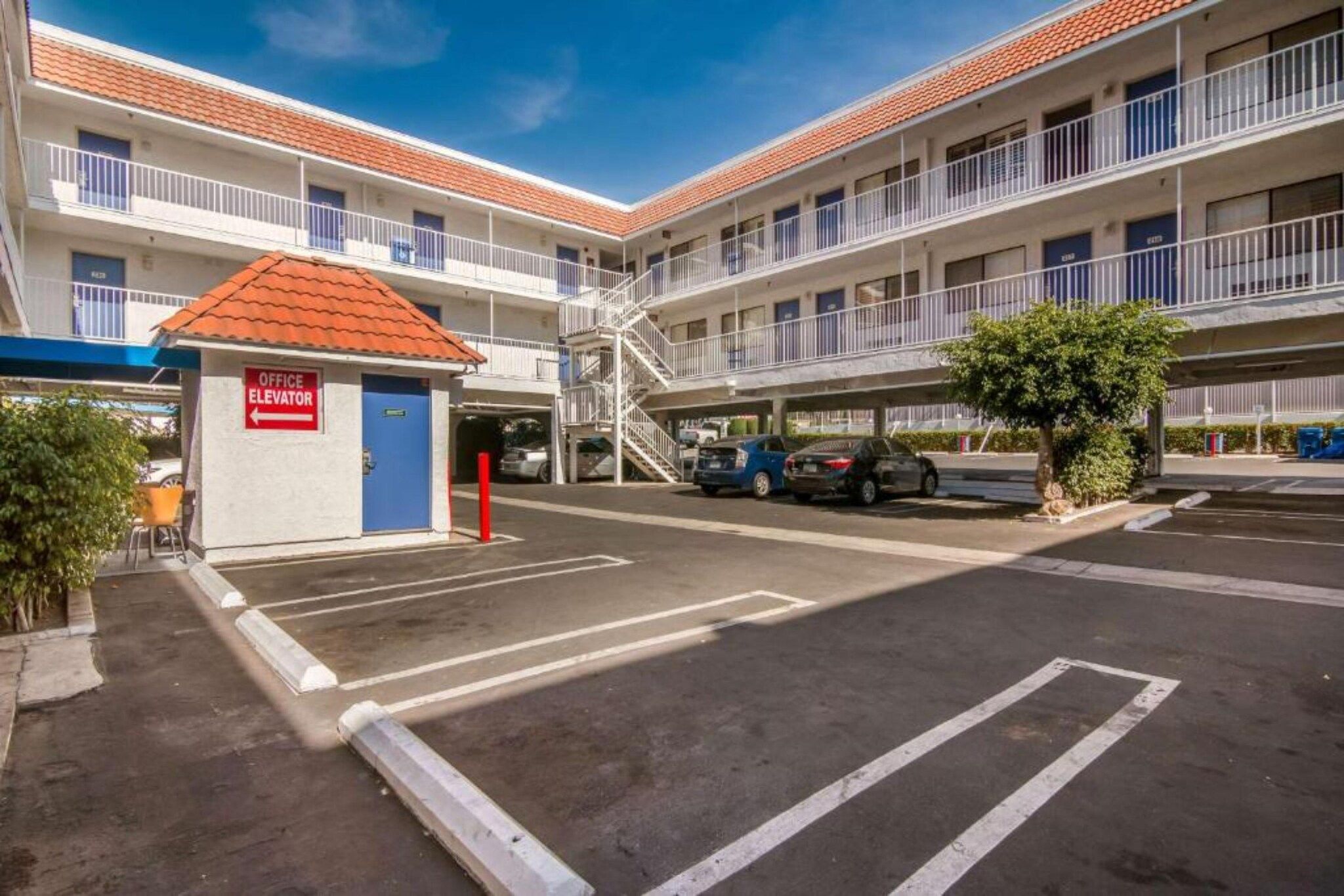 A multi-story building with a parking area, a small office with an elevator sign, and a staircase leading to the upper floors.