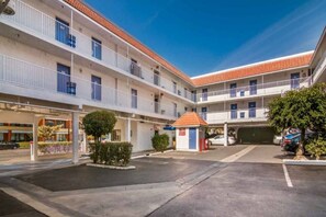 A multi-story hotel with a central courtyard, outdoor parking, and a small kiosk.