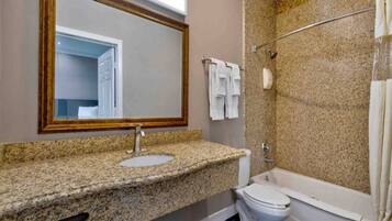A bathroom with a granite countertop sink, a toilet, a bathtub, and a shower with a glass door.