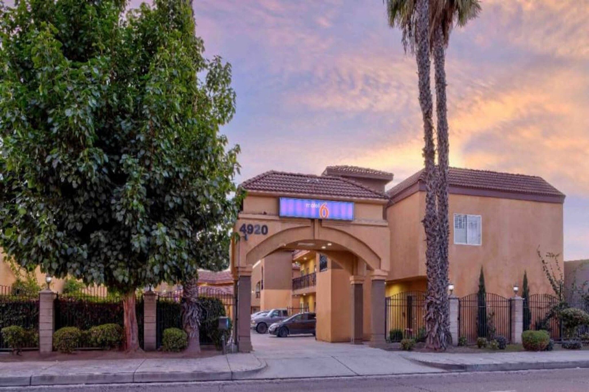 A hotel entrance with a large archway, a sign indicating the number 4920, and a parking area with cars.