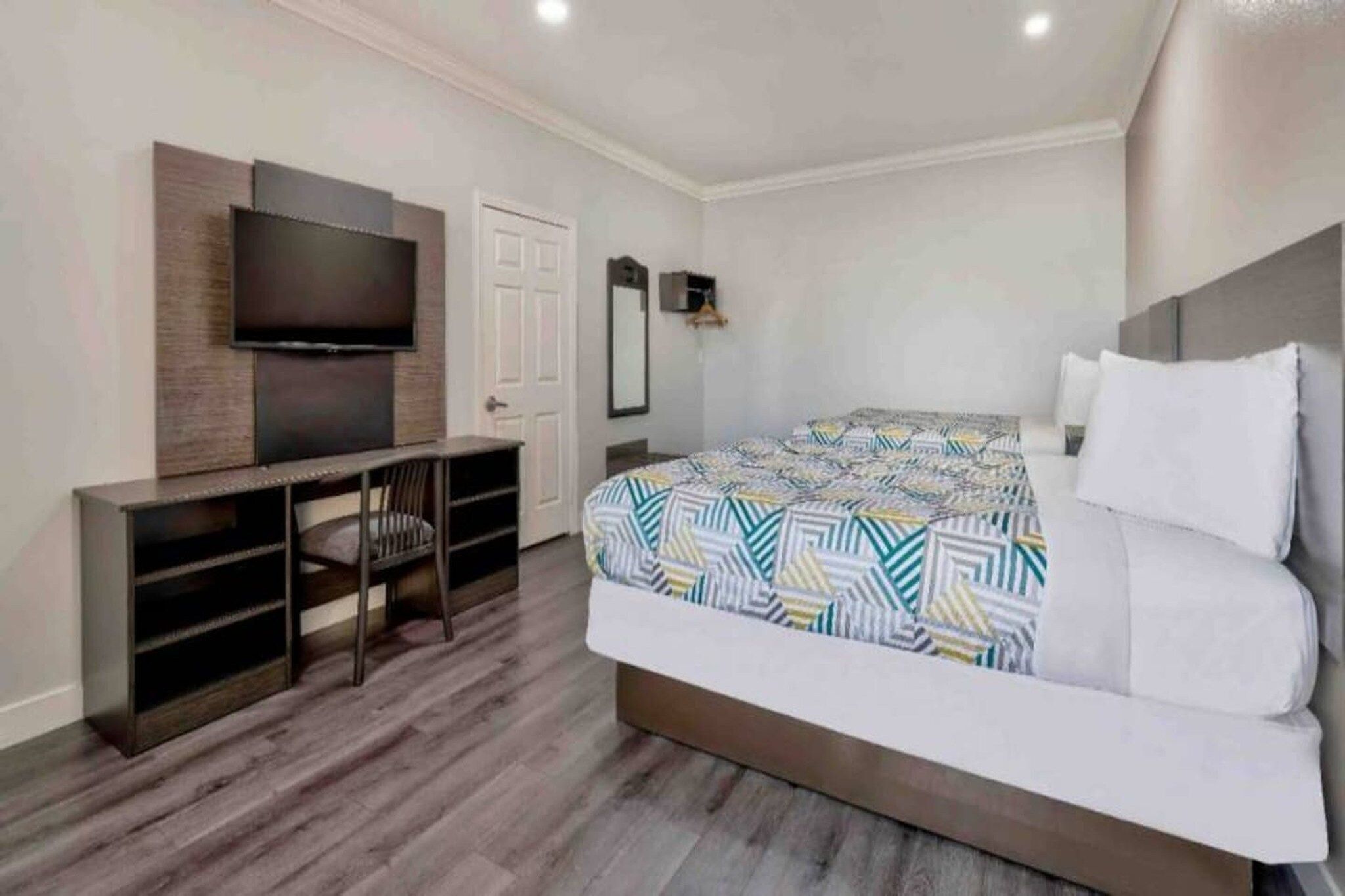 A modern bedroom with a bed, a TV mounted on a wall, and a desk with a chair.