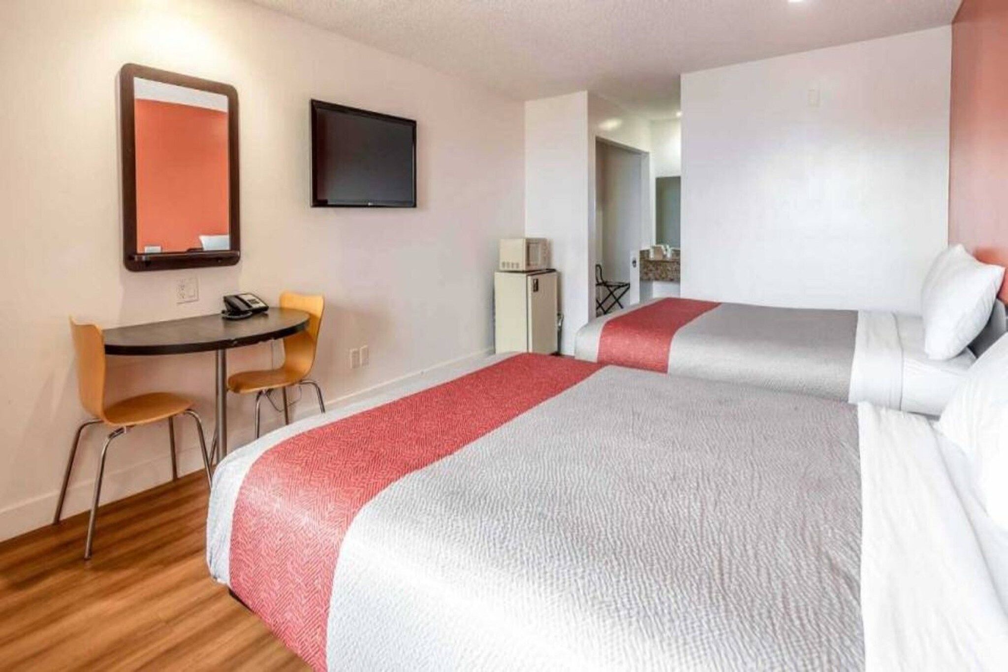 A hotel room with two beds, a desk, a chair, a television, and a microwave.