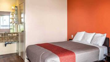 A hotel room with a bed, a bathroom with a mirror, and a red accent wall.