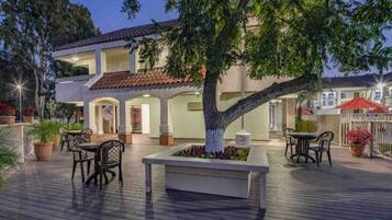 A hotel with a covered outdoor area featuring a central tree, seating arrangements, and a tiled roof.