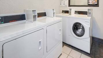 A laundry room with a front-loading washing machine and two dryers.