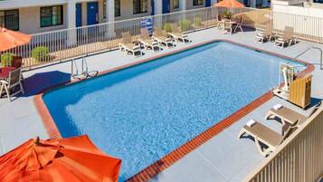 A rectangular swimming pool with a tiled deck, surrounded by lounge chairs and umbrellas.
