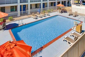 Piscina retangular com espreguiçadeiras e guarda-sóis ao redor de um deck revestido.