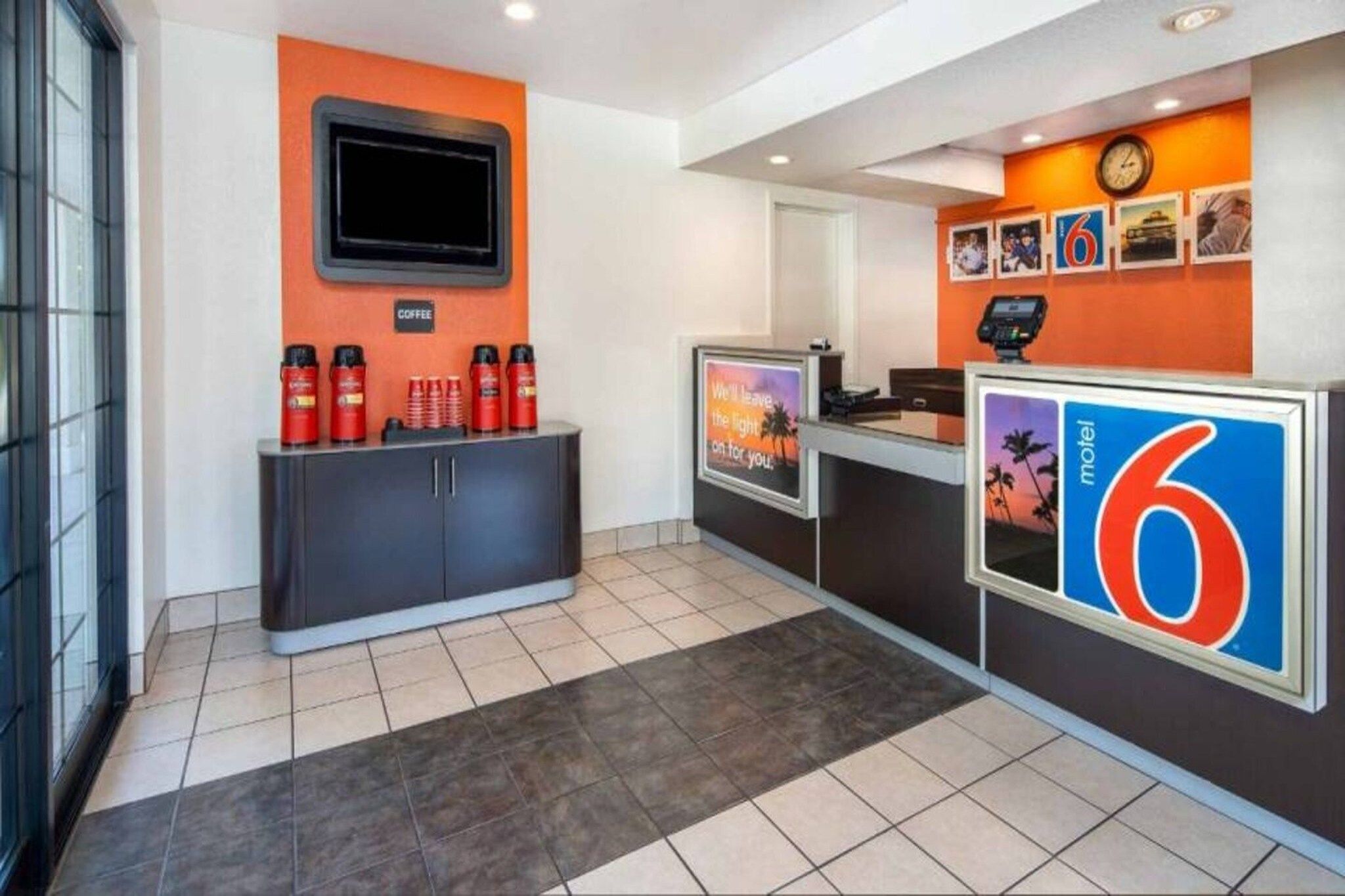 A hotel reception area with a coffee station, a TV screen, and a counter with a number sign.