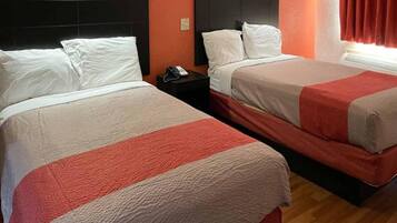Two beds with white and red bedding, a nightstand with a phone, and a window with curtains.