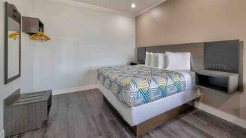 A modern hotel room with a bed, a nightstand, a mirror, and a wall-mounted TV.