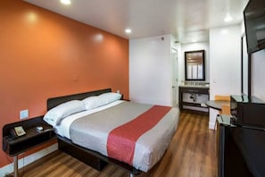 Une chambre d’hôtel avec un lit, une table de chevet et un petit bureau avec une chaise.