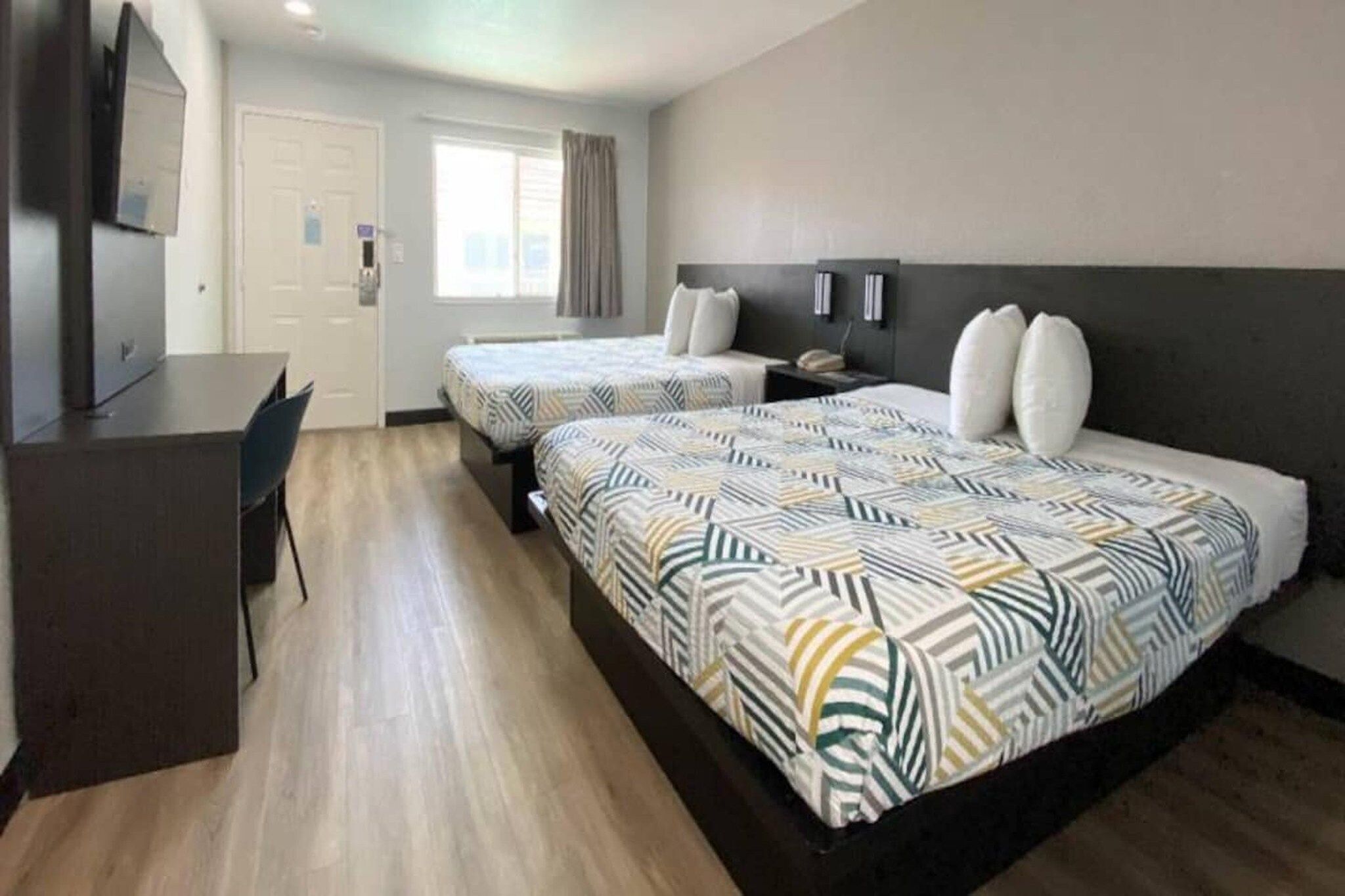 A hotel room with two beds, a desk, and a chair.