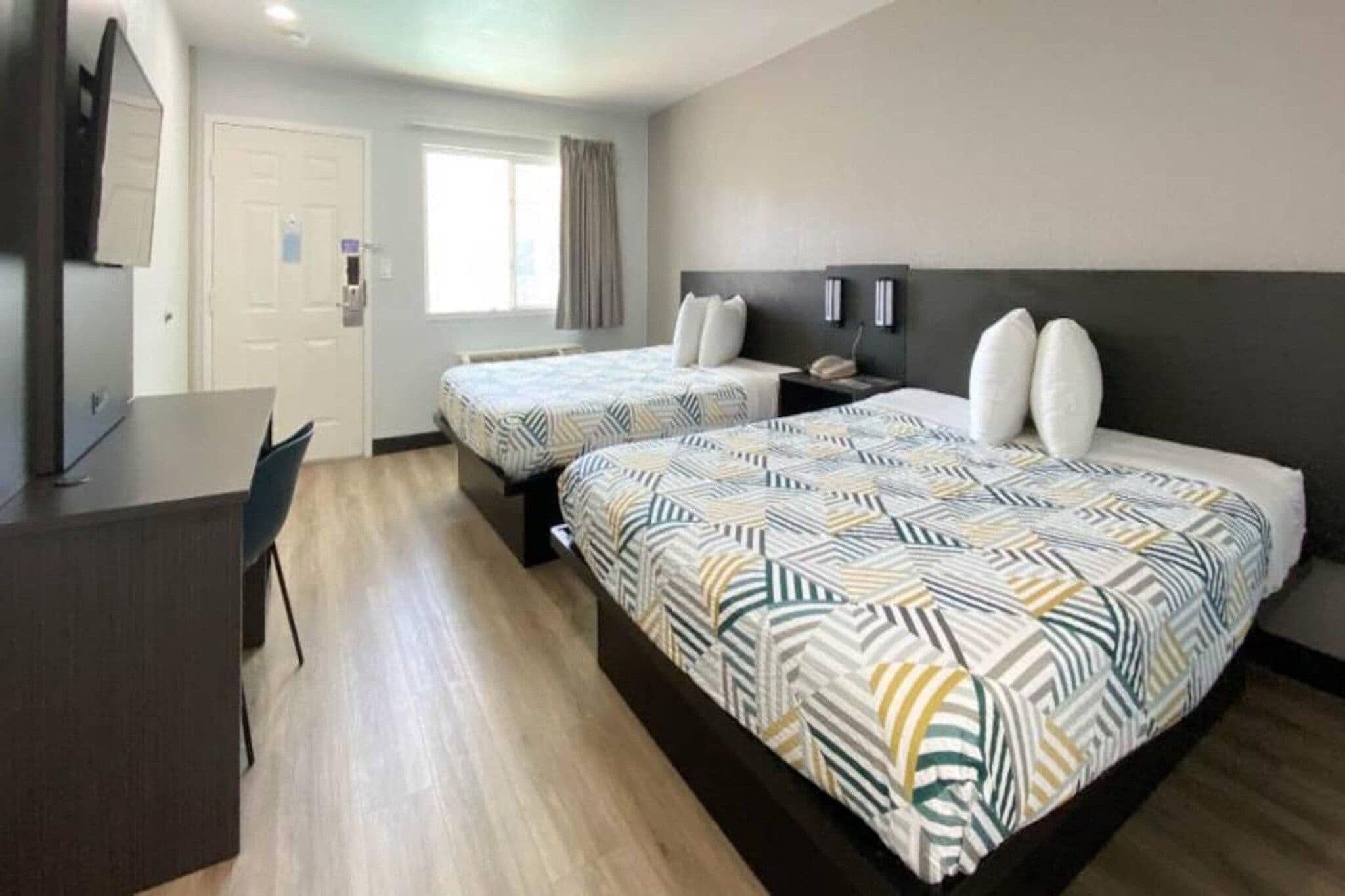 A hotel room with two beds, a desk, and a chair.