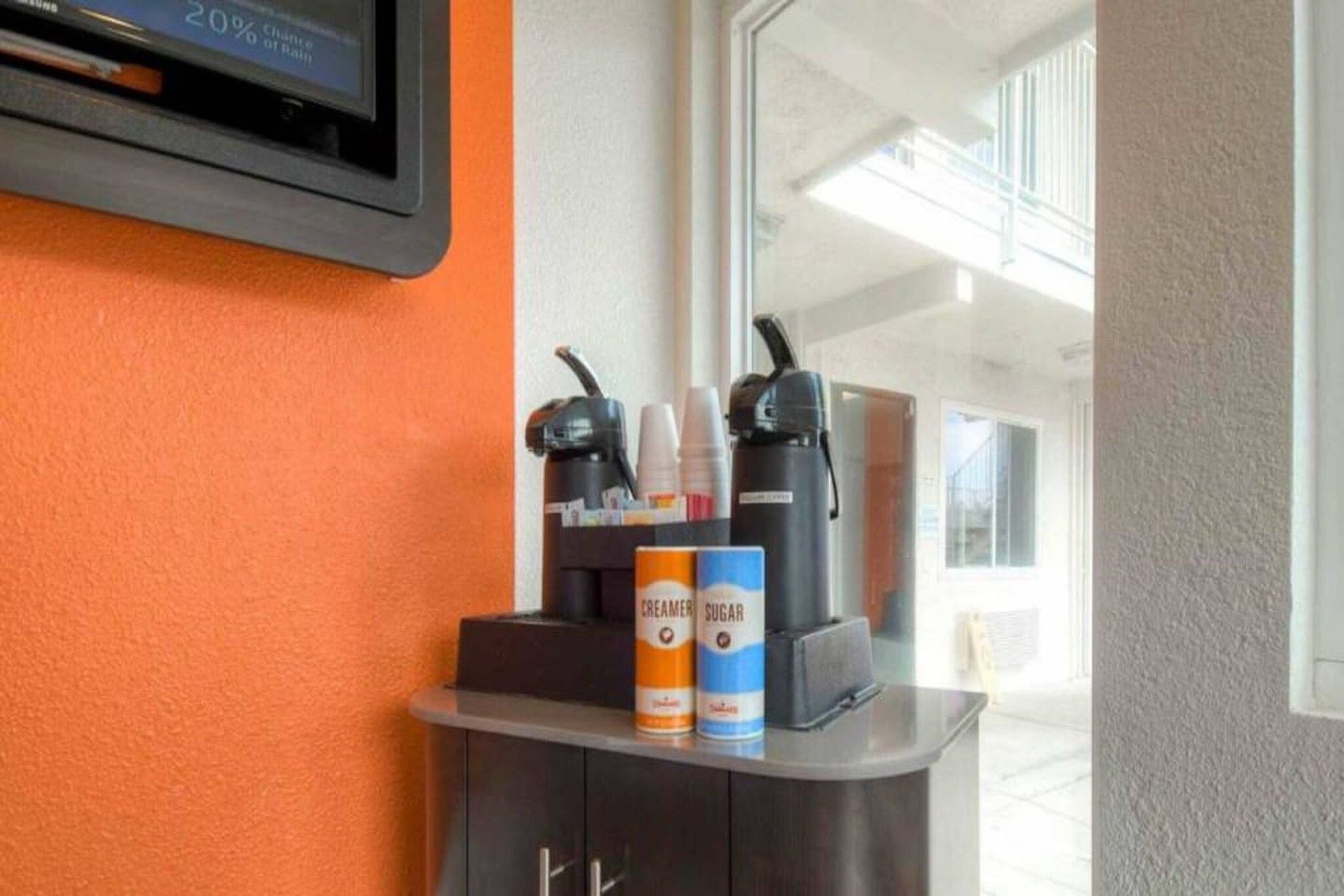 A coffee station with a coffee machine, cups, and creamer and sugar cans.