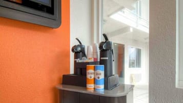A coffee station with a coffee machine, cups, and creamer and sugar cans.