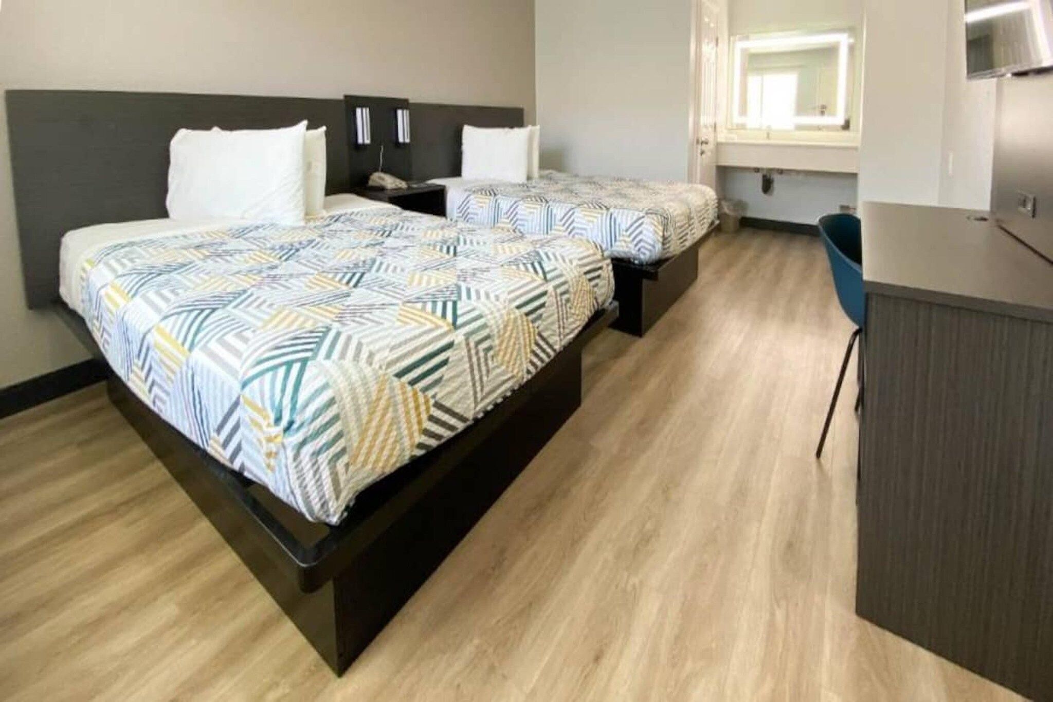 A hotel room with two beds, a desk, and a kitchenette.