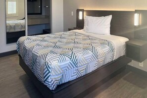 Een hotelkamer met een bed, nachtkastje, bedlampje en een inbouwkast met spiegel.