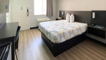 A hotel room with a bed, bedside table, lamp, and a desk with chairs.