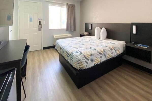 Een hotelkamer met een bed, nachtkastje, lamp en een bureau met stoelen.