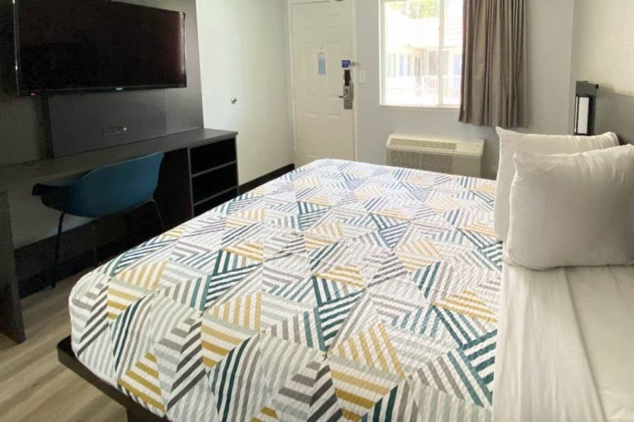 A hotel room with a bed, a TV, a desk, and a chair.