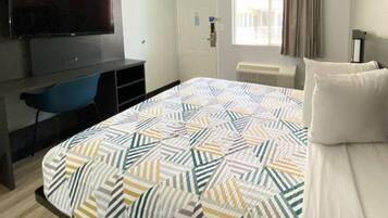 A hotel room with a bed, a TV, a desk, and a chair.