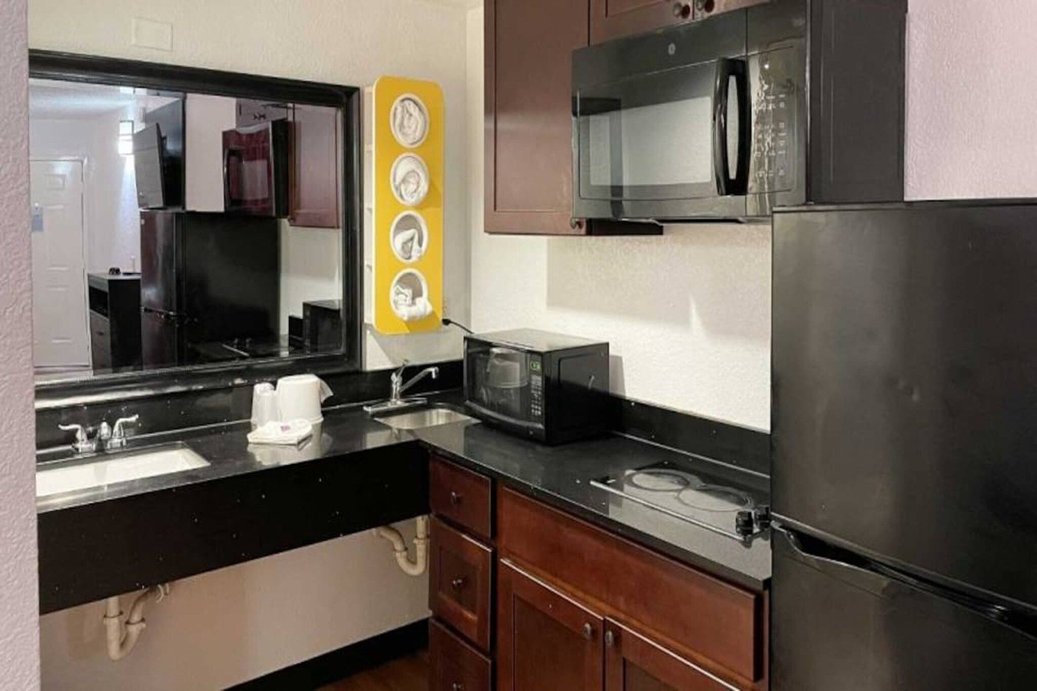 Una cocina compacta con refrigerador, microondas, pileta y un adorno amarillo en la pared.