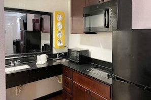 Una cocina compacta con refrigerador, microondas, pileta y un adorno amarillo en la pared.