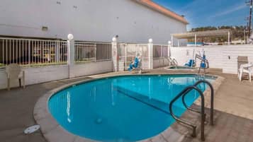 Piscina com escada de metal, cercada por uma cerca branca com luminárias.