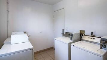 A laundry room with two washing machines and a dryer, white walls, and a tiled floor.