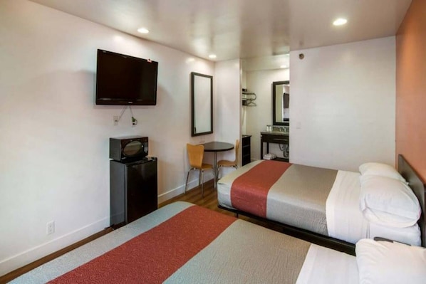 Une chambre d’hôtel avec deux lits, une télévision, un bureau avec un micro-ondes, une chaise et une petite table.