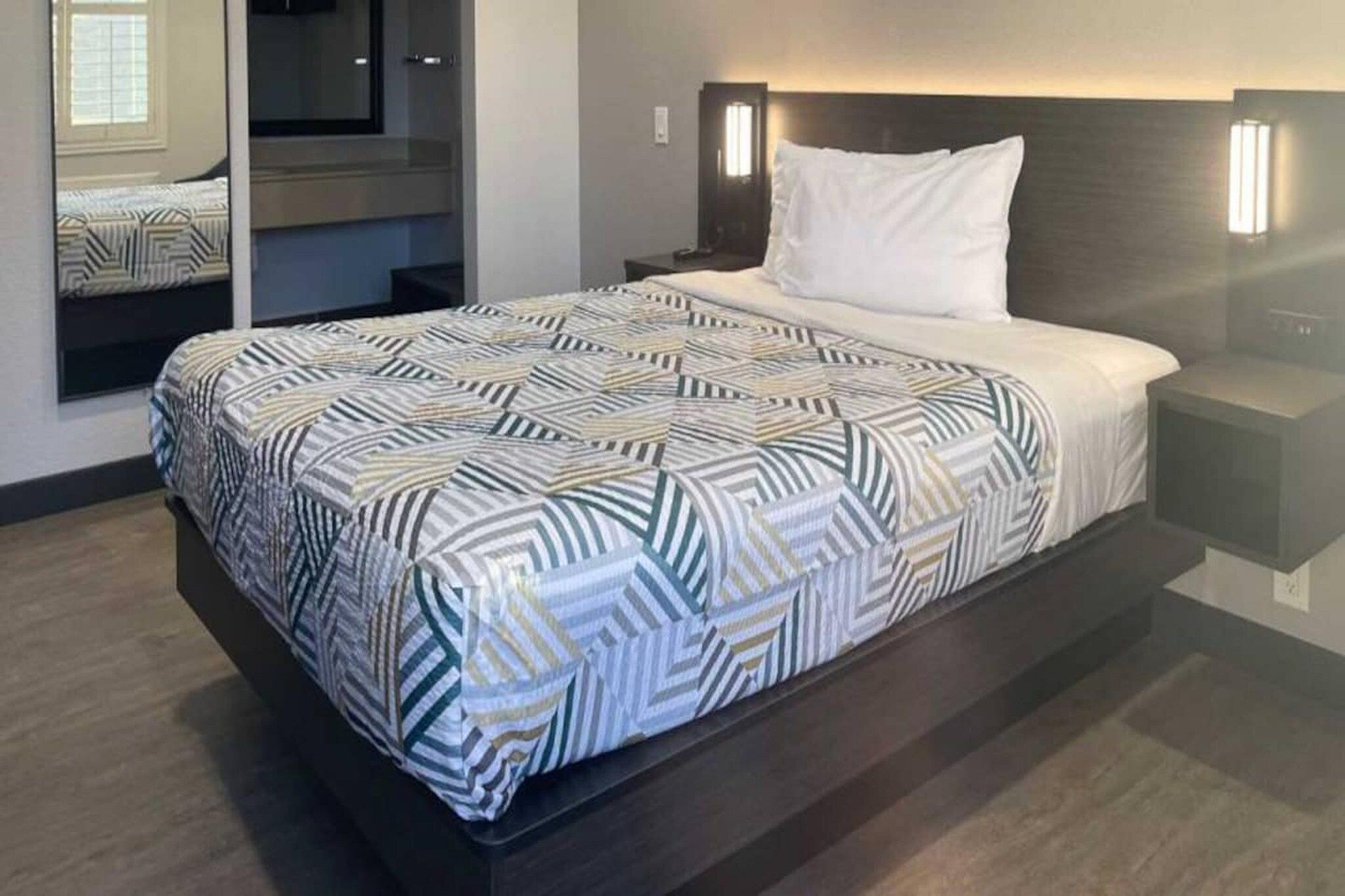A hotel room with a bed, a nightstand, a bedside lamp, and a built-in closet with a mirror.
