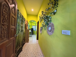 A hallway with a yellow wall, a wooden door with intricate carvings, and a wall-mounted light switch.