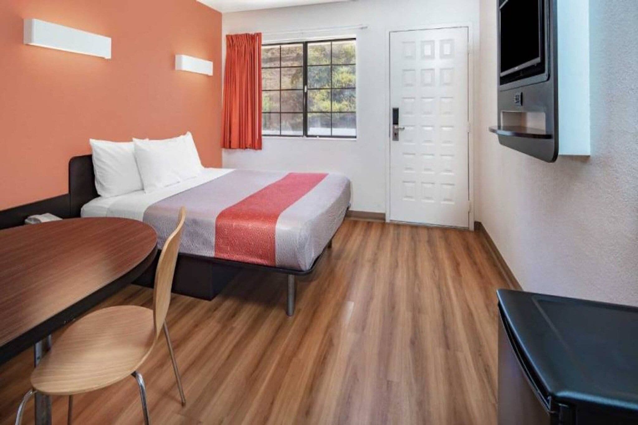 A hotel room with a bed, a desk, a chair, a TV, and a door.