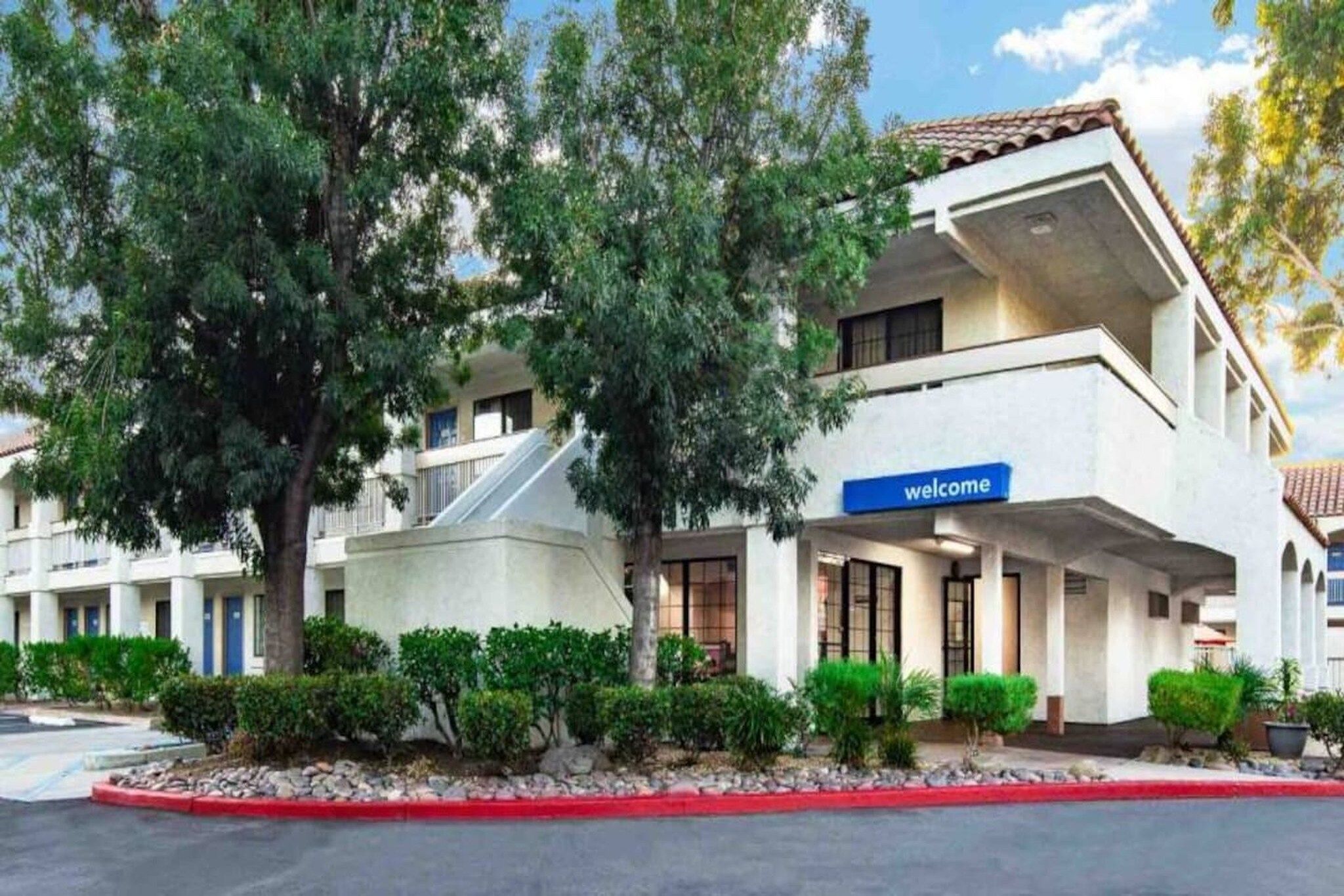 Un edificio de varios pisos con un letrero que dice 'welcome', rodeado de árboles y arbustos.