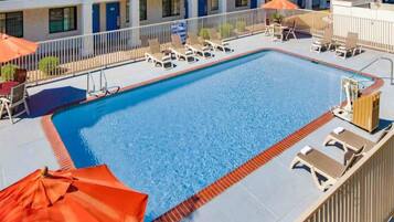 A swimming pool with lounge chairs and umbrellas, surrounded by a building with balconies.